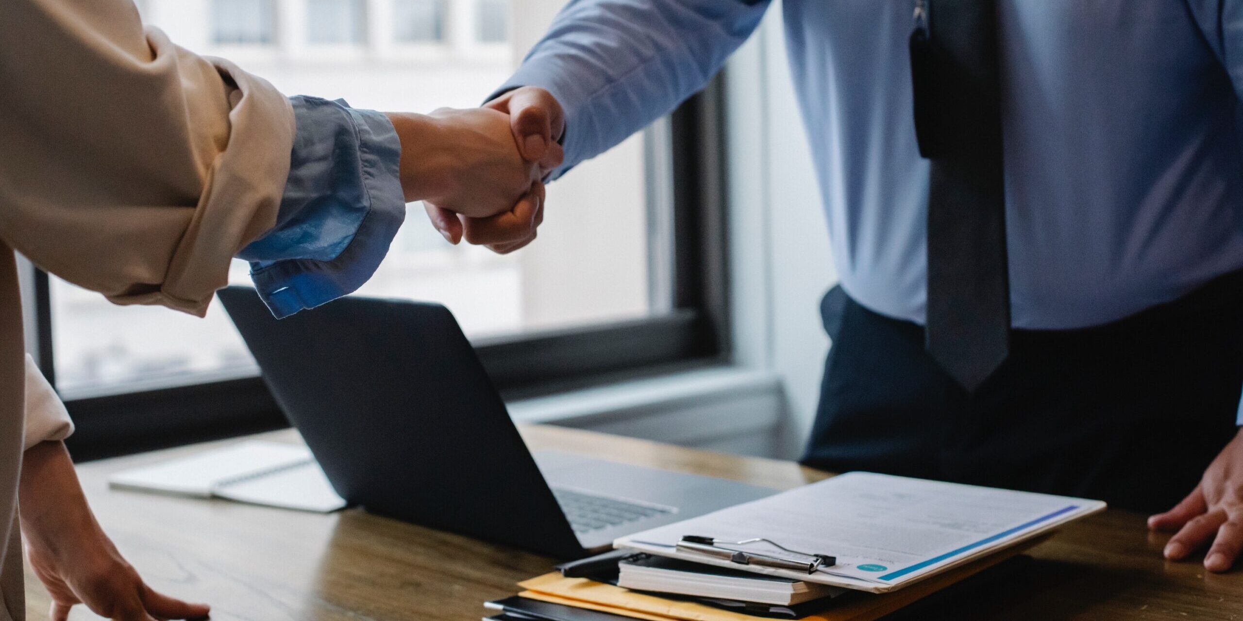 two people shaking hands over a laptop and some documents